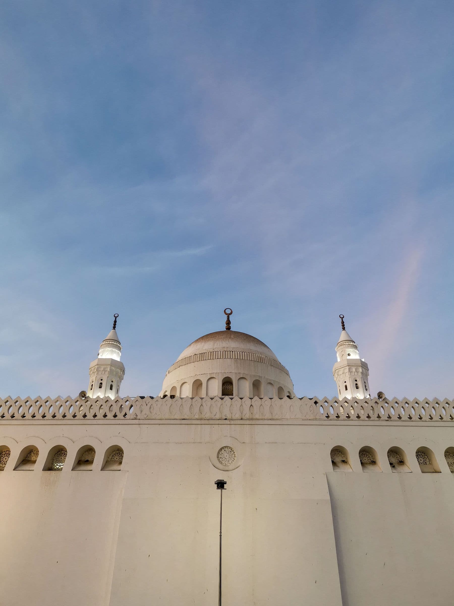 Masjid al-Qiblatayn dome and twin minarets over white wall, soft blue sky